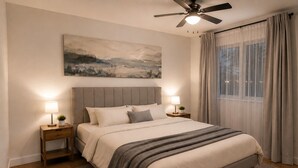 A bedroom with a bed, two bedside tables, a ceiling fan, a painting on the wall, and a window with curtains. - Luxury apartment 3BR (Longueuil)