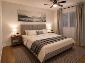 A bedroom with a bed, two bedside tables, a ceiling fan, a painting on the wall, and a window with curtains.