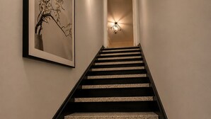 A staircase with a framed artwork on the wall, a light fixture above the door, and a textured floor. - Luxury apartment 3BR (Longueuil)