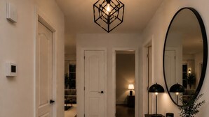 A hallway with a geometric light fixture, a large mirror, a console table with a vase, and a rug. - Luxury apartment 3BR (Longueuil)