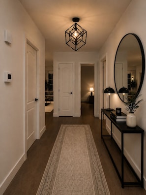 A hallway with a geometric light fixture, a large mirror, a console table with a vase, and a rug.