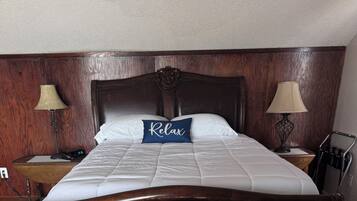 Ein ordentlich bezogenes Bett mit einem Kissen, auf dem 'Relax' steht, in einem Hotelzimmer mit Holzvertäfelung und zwei Nachttischlampen.