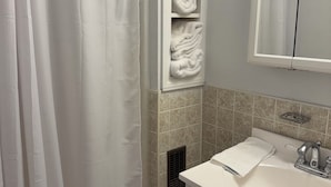 Un baño con cortina de ducha, toallero, lavabo con espejo y estante para toallas.