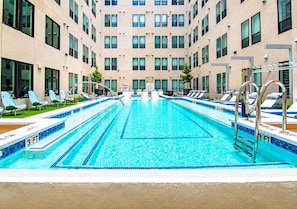 A swimming pool with lounge chairs and a multi-story building in the background. - Sleek DT Studio | Rooftop Pool & Gym Access (Houston)