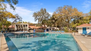 A swimming pool with lounge chairs, surrounded by trees and buildings.