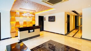 A hotel reception area with a modern design, including a reception desk, a wall-mounted TV, and a marble floor. - Suite Palette South Delhi Imperial Villa (New Delhi)