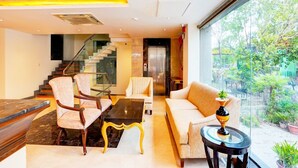 A modern hotel lobby with a staircase, seating area, and a view of the outdoors. - Suite Palette South Delhi Imperial Villa (New Delhi)