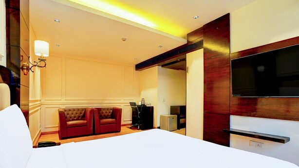A hotel room with a large bed, a TV, a desk with a chair, and a sofa. - Suite Palette South Delhi Imperial Villa (New Delhi)