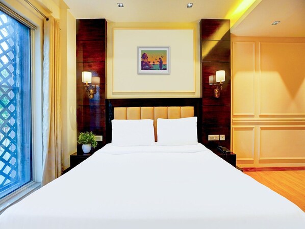 Habitación de hotel con una cama grande, una mesita de noche con lámpara, un cuadro colgado en la pared y una ventana con cortinas.