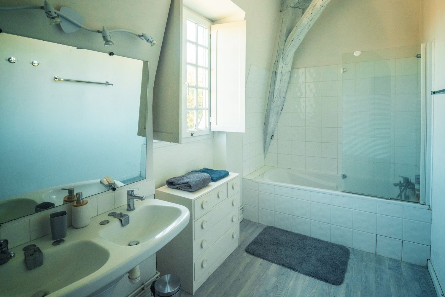 Un baño con lavamanos, espejo, tocador y zona de ducha.