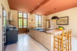 A kitchen with a central island, wooden cabinets, a black countertop, and a dining area with wooden chairs.