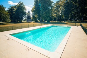 Une piscine rectangulaire à l’eau d’un bleu limpide, entourée d’une terrasse carrelée et d’une clôture.