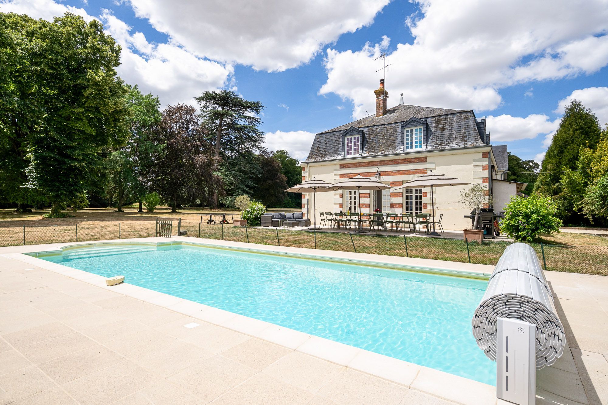 Una casa con piscina, muebles de exterior y jardín vallado.