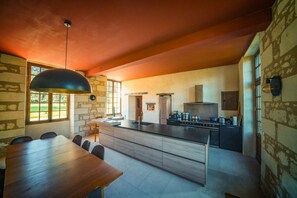 A modern kitchen with a central island, a dining area with a wooden table and chairs, and a stone wall.