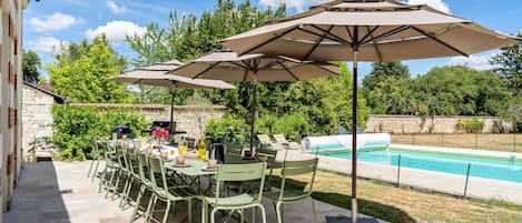 An outdoor patio with a pool, green metal chairs, and umbrellas.