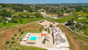 Vista aérea de una propiedad con piscina, un edificio pequeño y un grupo de casas con techos cónicos.