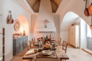 A dining area with a wooden table set for a meal, a kitchen area with cabinets, and a hanging light fixture. - Masseria Zia Cocca - Five Bedroom Villa, Sleeps 10 (Martina Franca)