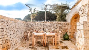 Un área de comedor al aire libre con paredes de piedra, una mesa dispuesta para dos personas, suelo de piedra y un ambiente rústico.