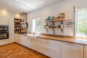 A kitchen with white cabinets, a built-in oven, and a window with a view of greenery. - Villa Chautard - Four Bedroom Villa, Sleeps 8 (Tourrettes)