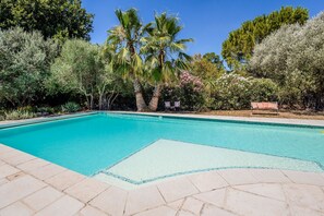 A clear blue swimming pool with tiled edges, surrounded by various trees and shrubs, and a bench on the right side. - Villa Chautard - Four Bedroom Villa, Sleeps 8 (Tourrettes)