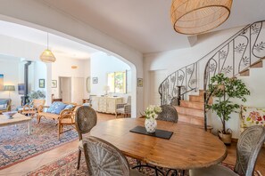 A spacious living area with a wooden dining table, wicker chairs, and a staircase with decorative railings. - Villa Chautard - Four Bedroom Villa, Sleeps 8 (Tourrettes)
