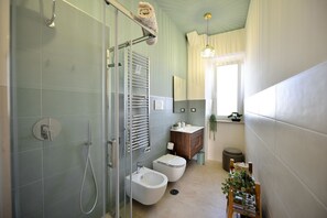 A bathroom with a glass-enclosed shower, a wooden vanity, a bidet, and a small potted plant.