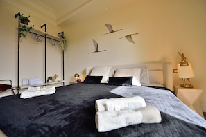 A neatly made bed with a black and white quilt, a bedside table with a lamp, and a wall with bird silhouettes.