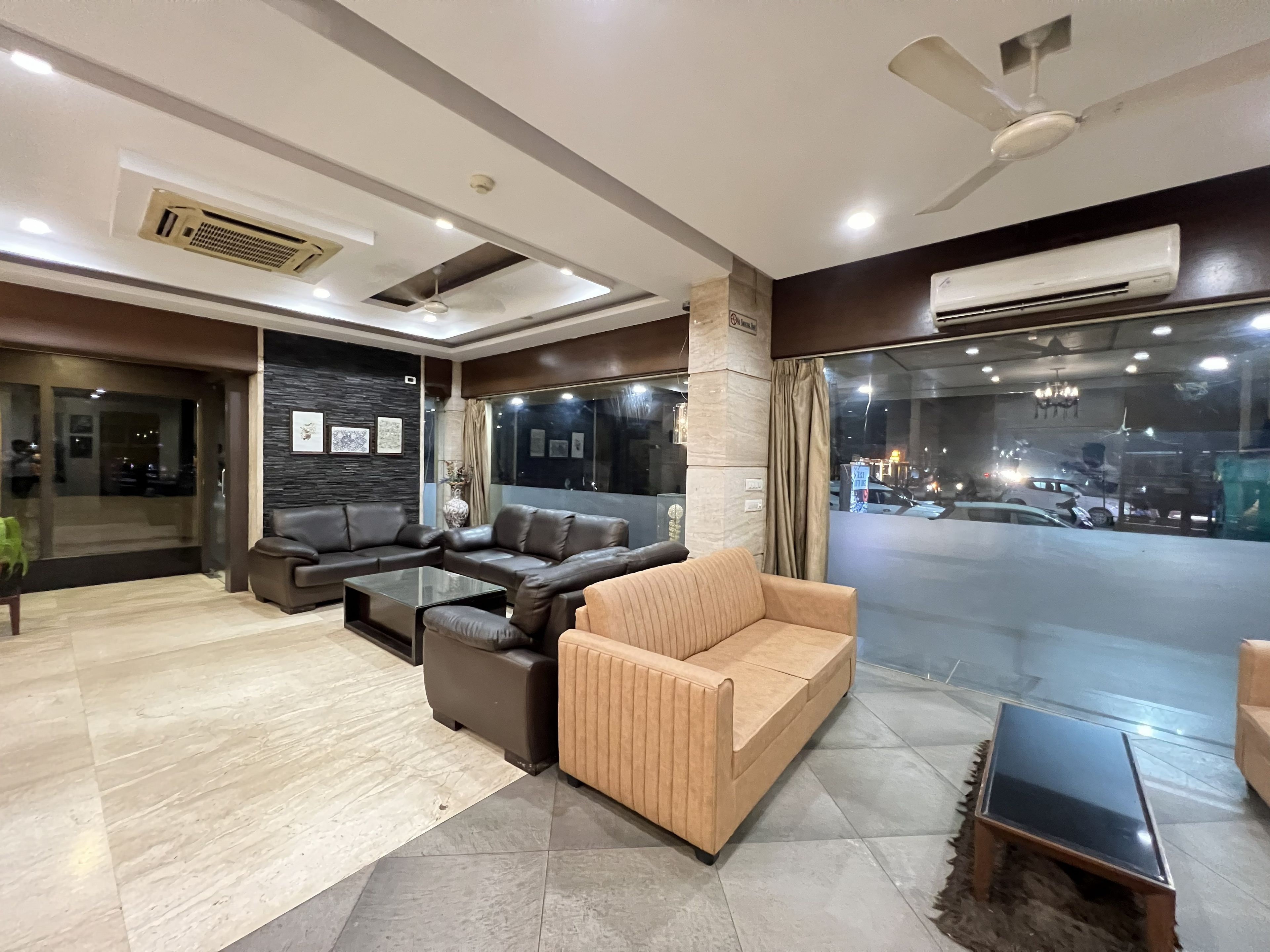A modern living room with leather sofas, a glass coffee table, and a view of the street through large windows.