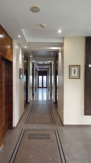A long, well-lit hallway with a polished floor, wooden paneling on one side, and a framed picture on the wall. - Hotel Surya Palace  (Durg)