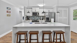 A kitchen with a large island, bar stools, pendant lights, and a microwave.