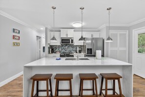 A kitchen with a large island, bar stools, pendant lights, and a microwave.