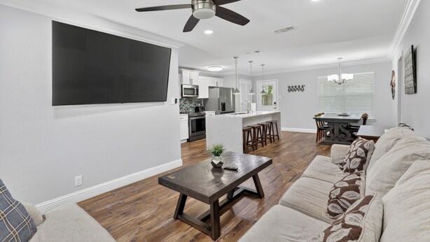 A modern living room with a sofa, a coffee table, a ceiling fan, and a kitchen area in the background.