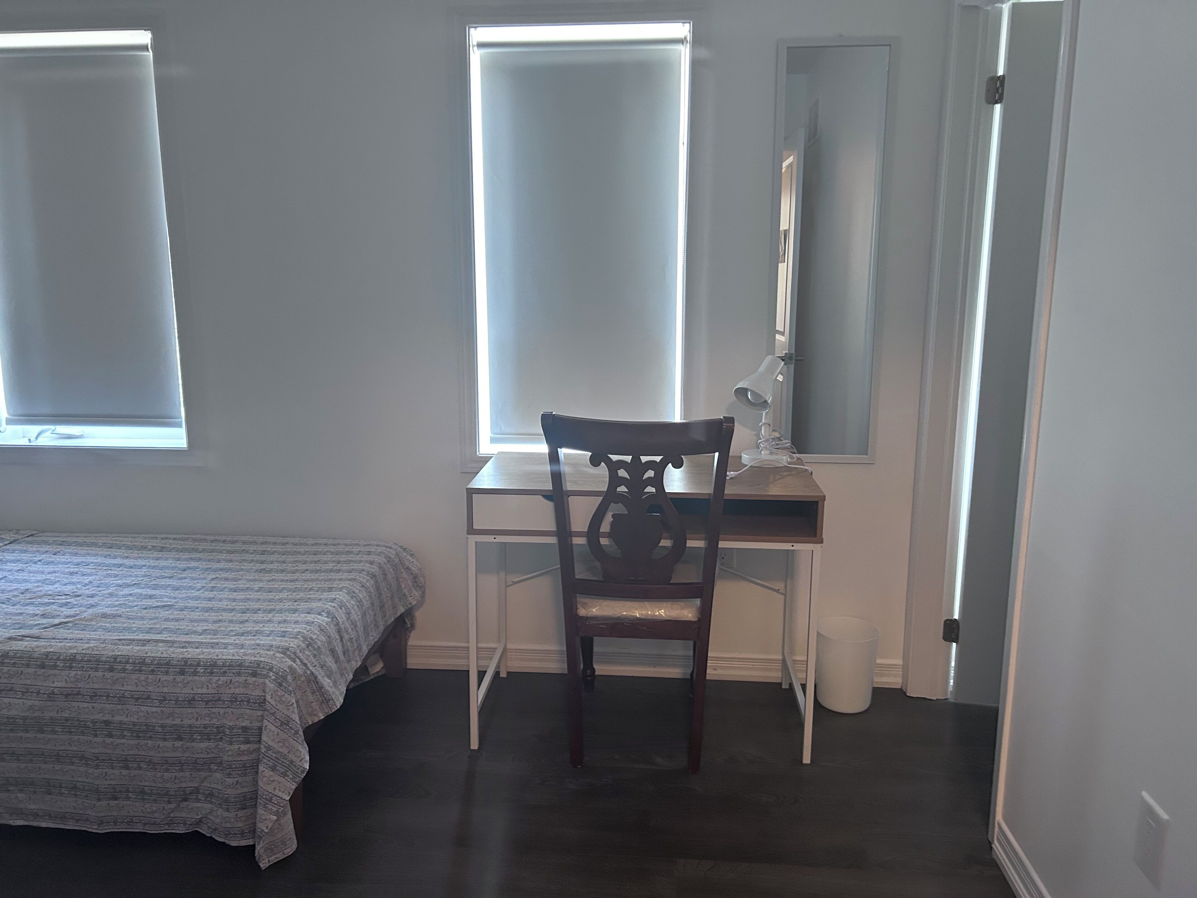 A bedroom with a bed, a desk, a chair, a mirror, and a window.