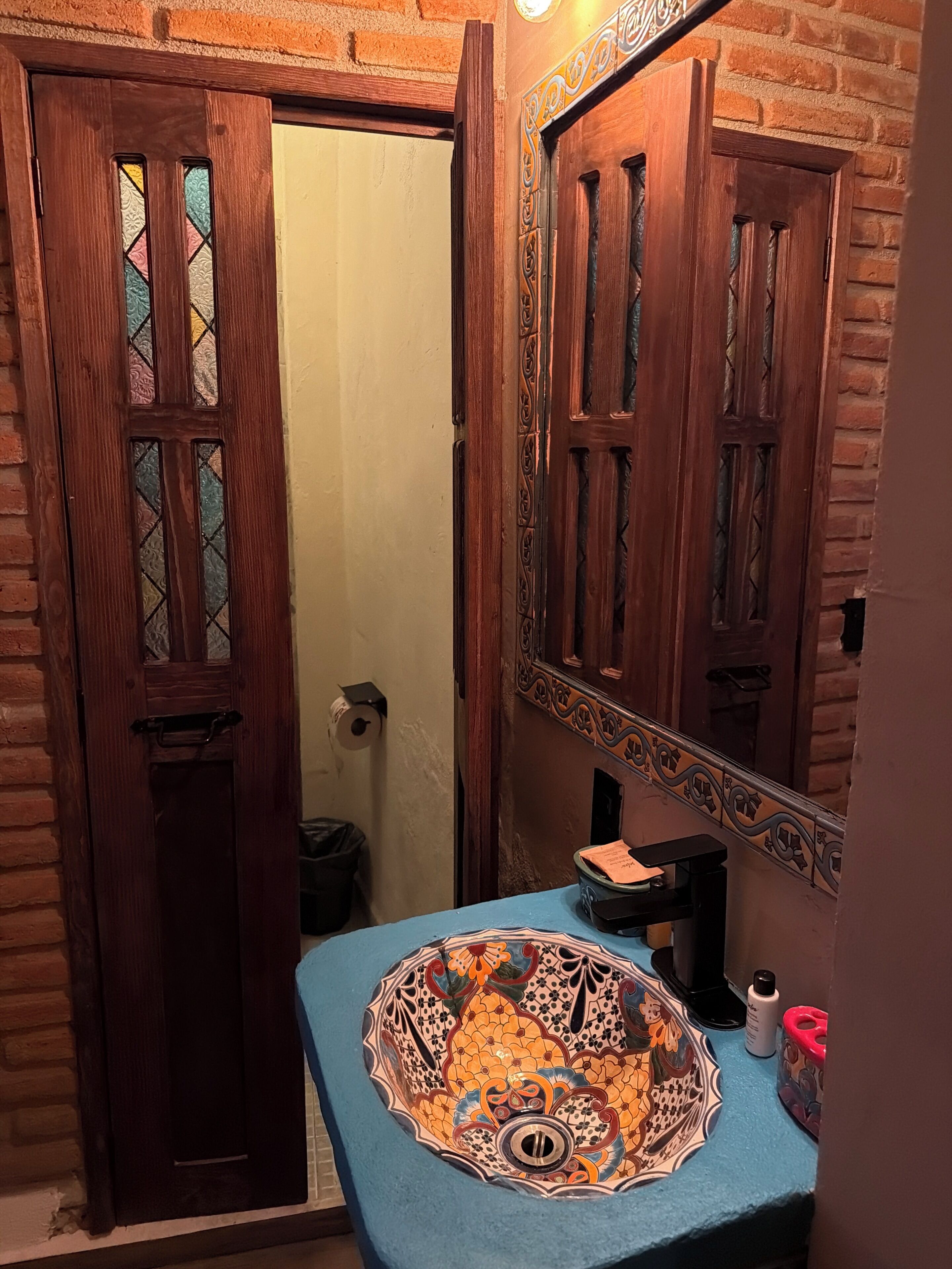 A bathroom with a wooden door, a mirror, a sink with a decorative tile basin, and a toilet.