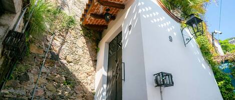 Un edificio blanco con pared de piedra, una reja de metal y una ventana pequeña.