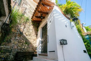 Un edificio blanco con pared de piedra, una reja de metal y una ventana pequeña.