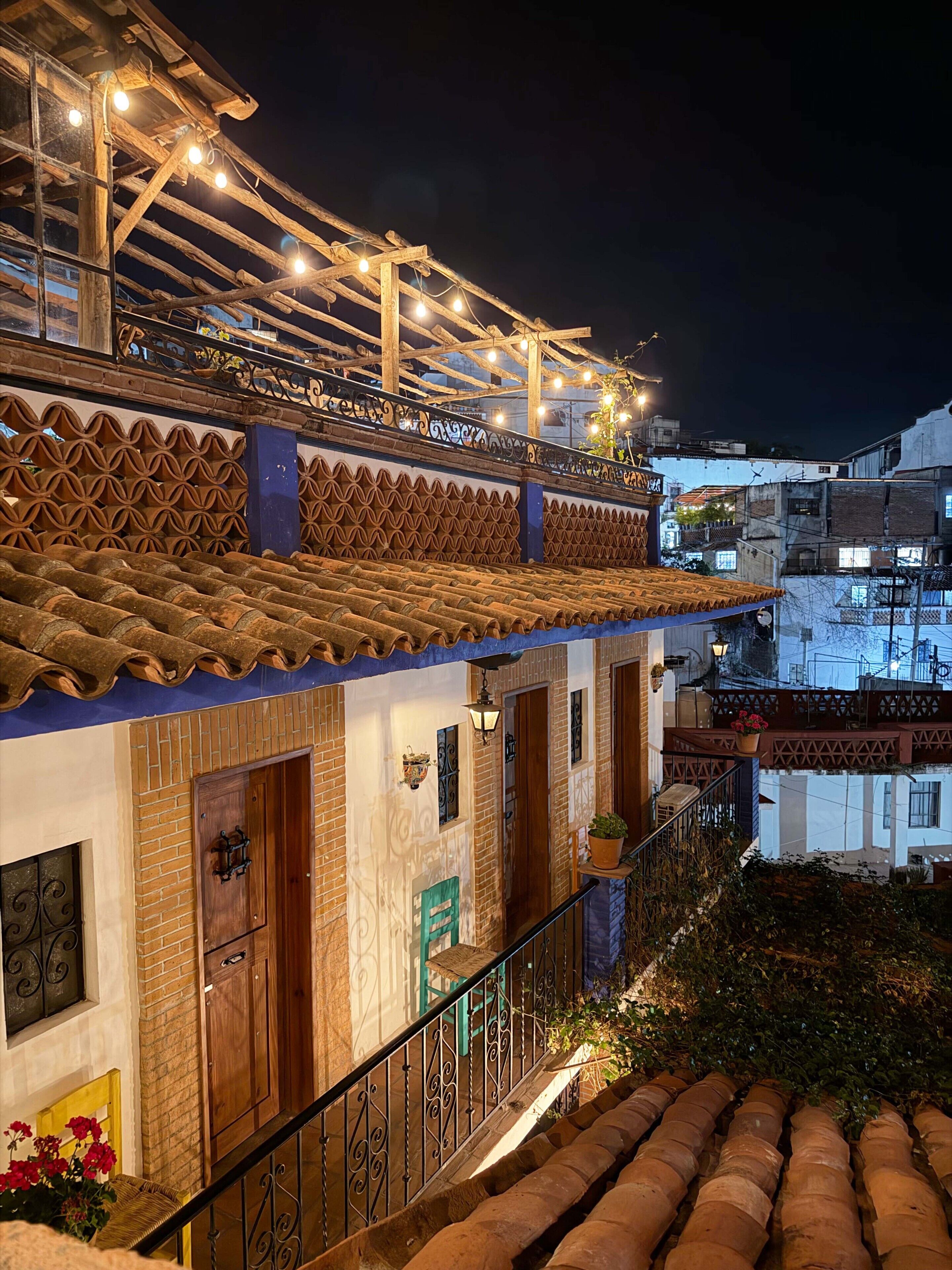A building with a tiled roof, a balcony with string lights, a wooden door, and a staircase with a railing.
