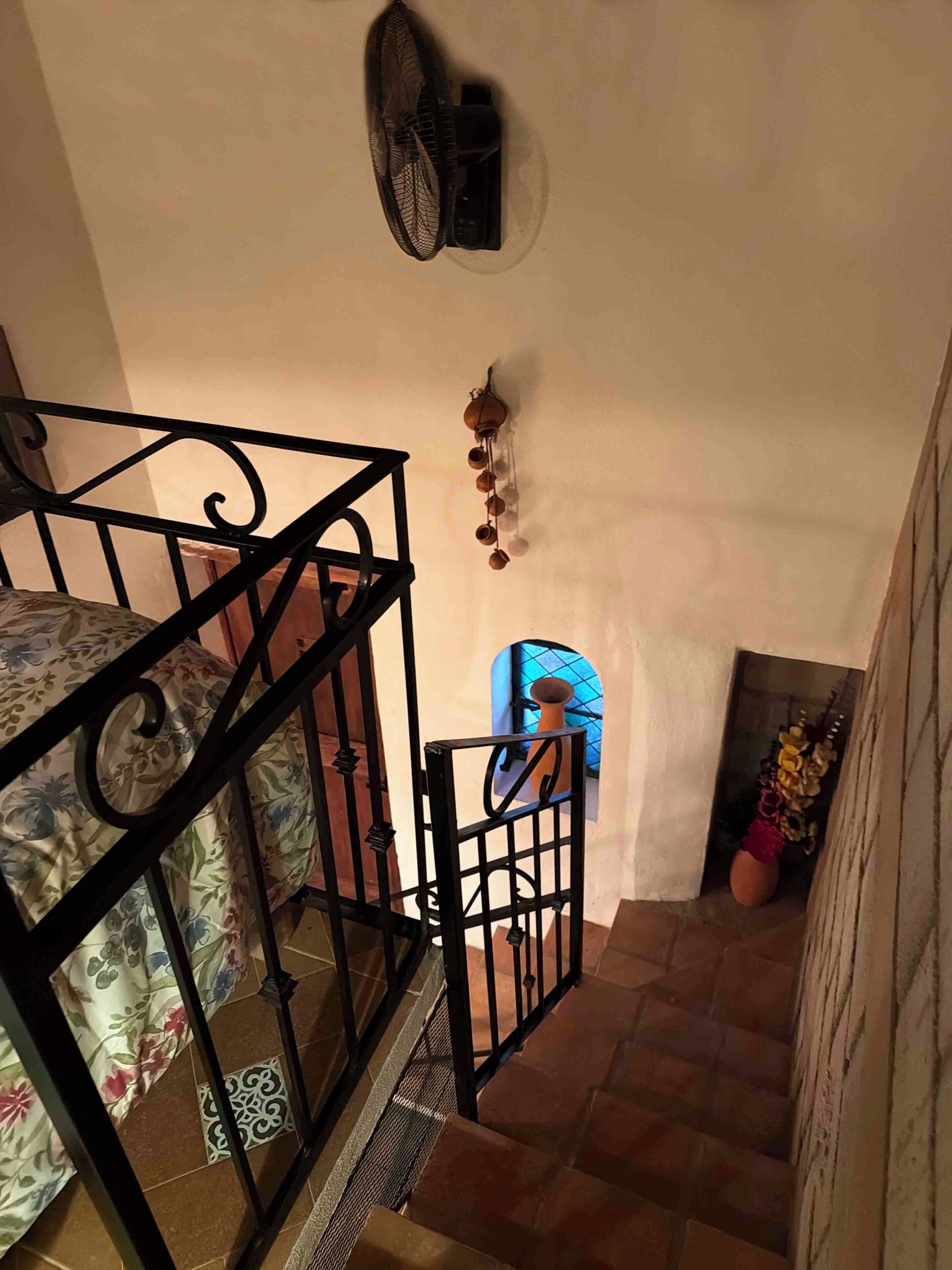 Un escalier avec une rampe en métal, un ventilateur fixé au mur et une petite fenêtre donnant sur le paysage.