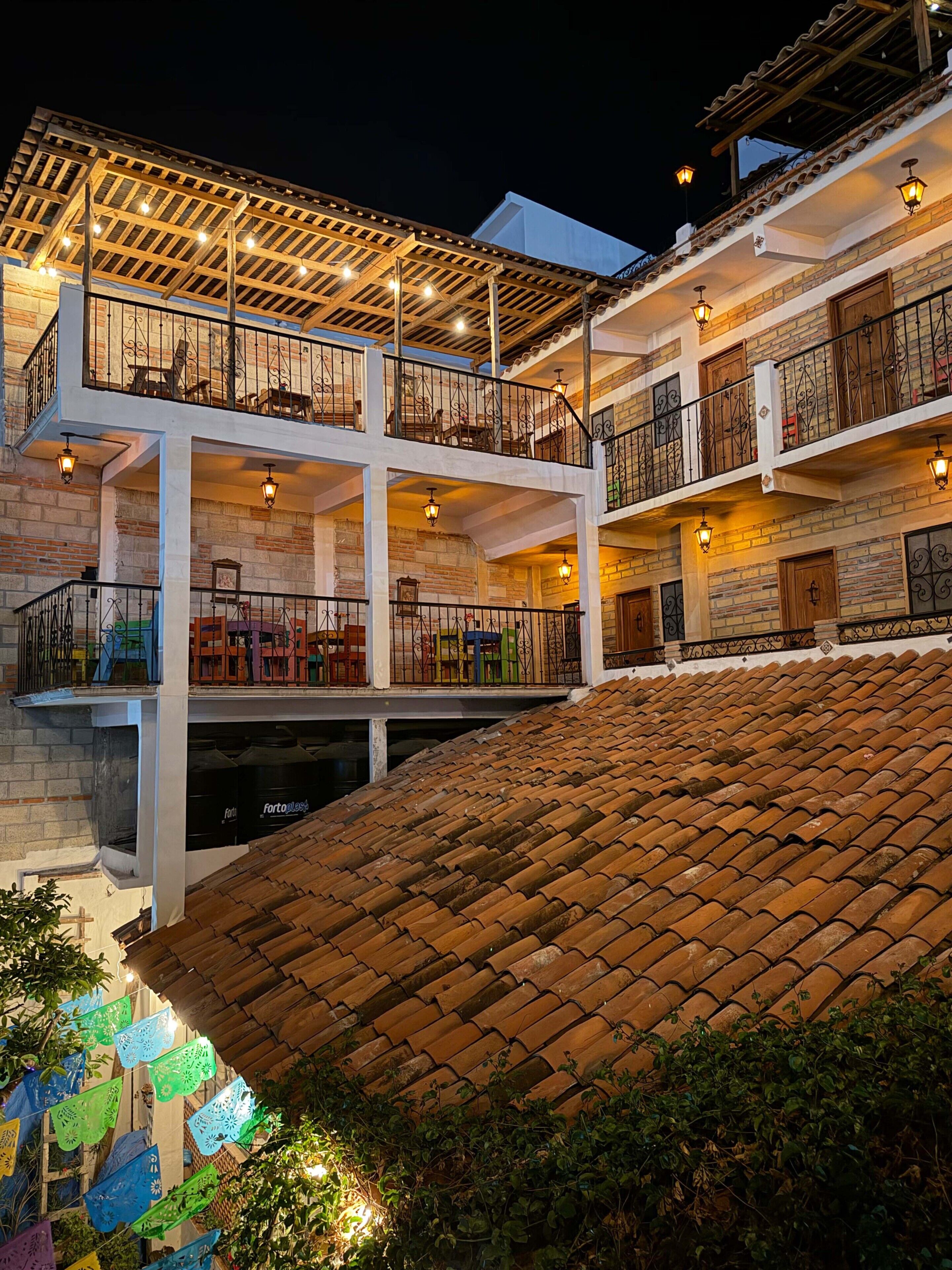 Un edificio de varios pisos con balcones, mobiliario exterior y techo de tejas.