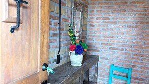 A wooden door with a metal handle, a brick wall, a small table with a crocheted vase, a blue chair, and a woven chair. - La Casona de Los Angeles de San Juan (Taxco)