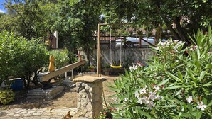 Ein Garten mit einer Holzschaukel, einer Steinsitzbank und verschiedenen Pflanzen.