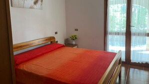 Ein Schlafzimmer mit einem Bett, einer Wandleuchte, einem kleinen Tisch mit einer Vase und einer Glastür zum Außenbereich.
