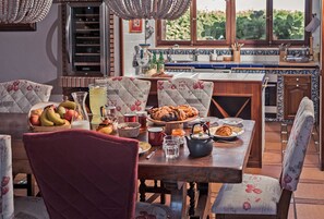 A dining area with a wooden table, floral chairs, and a view of the kitchen through a window.