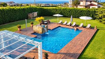 A rectangular swimming pool with a waterfall feature, surrounded by a wooden deck and lounge chairs.