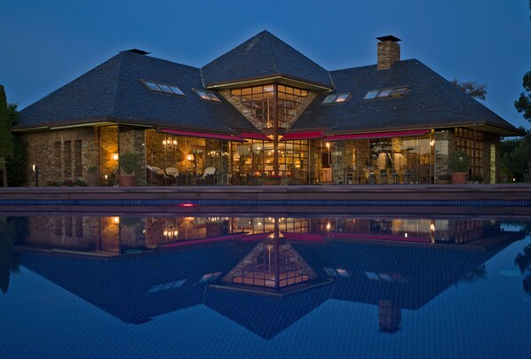 A large building with a swimming pool in front, featuring a prominent glass facade and a stone exterior.