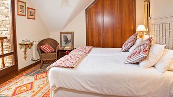 A bedroom with a large bed, a wooden wardrobe, a chair, a small table, and a patterned rug.
