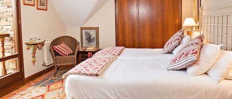 A bedroom with a large bed, a wooden wardrobe, a chair, a small table, and a patterned rug.