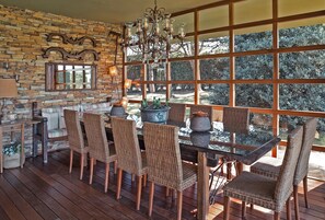 A dining area with wicker chairs, a glass table, and a stone wall.