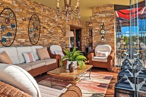 Una habitación con pared de piedra, muebles de mimbre, un candelabro y vistas amplias a través de grandes ventanales.