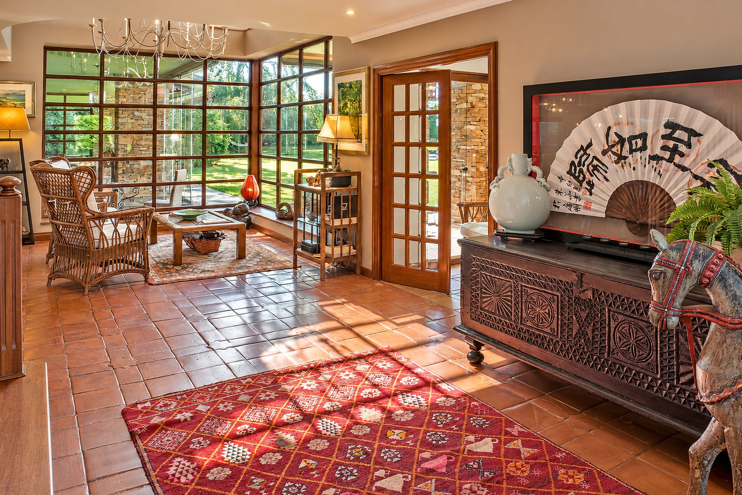 A spacious living room with a large window, a traditional Asian-style cabinet, and a red patterned rug.